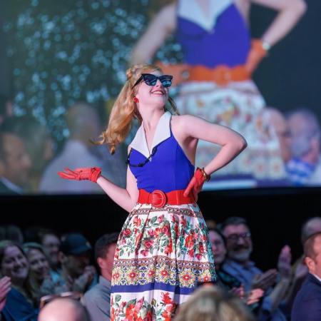 picture of a model on the runway at the 2024 GCC fashion show wearing a halter dress with a flowered skirt and red gloves